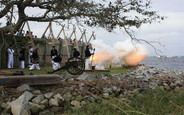men in historic uniforms firing cannon with flame and smoke and crowd looking along fence at fort caroline national memorial jacksonville