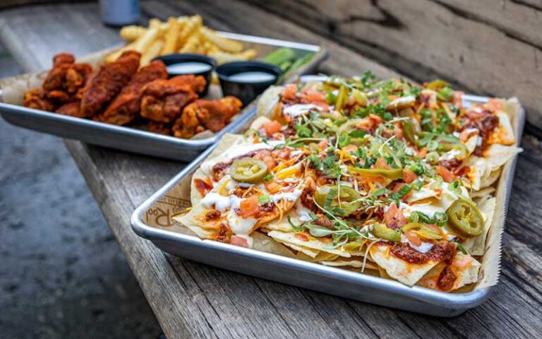 metal trays with loaded nachos and hot wings on wood bench at tin roof orlando icon park