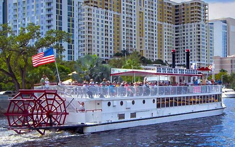 riverboat with paddle wheel and crowd on deck cruising by buildings at carrie b cruises ft lauderdale