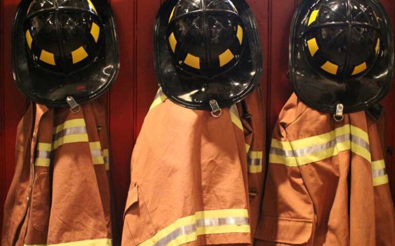 row of three firemen hats and coats hung on wall at fort lauderdale fire safety museum