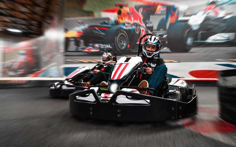 two karts racing around corner blurred with racing mural in background at k1 speed indoor kart racing jacksonville