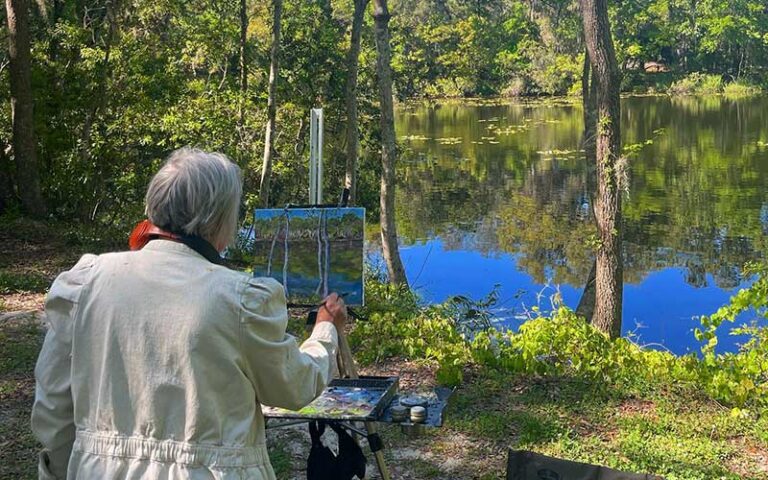woman painting facing pond scene with easel at jacksonville arboretum botanical gardens