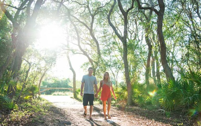 young couple walking hand in hand on forest trail at little talbot island state park jacksonville