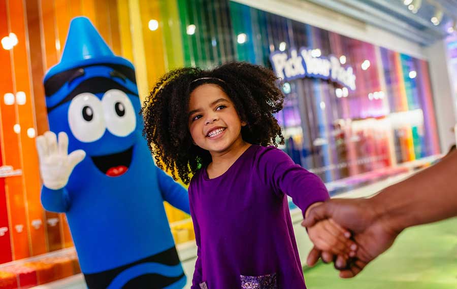 young girl holding hand in front of blue crayon character at crayola experience