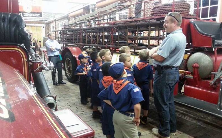 boy scout troop with fireman tour guide standing between trucks at orlando fire museum