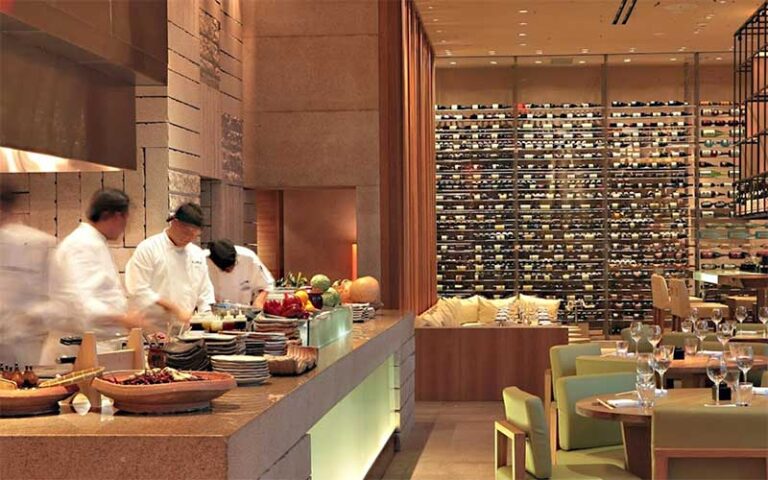chefs preparing sushi in open kitchen with dining area and wine racks at zuma miami