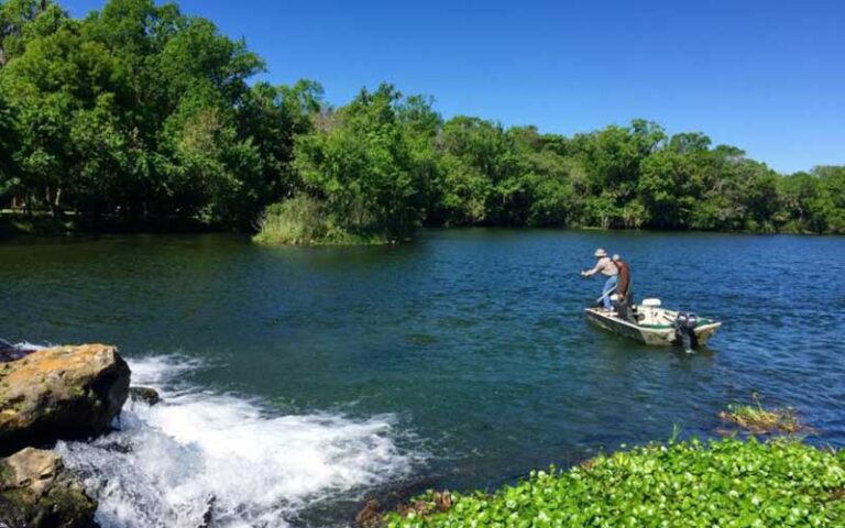 fishermen casting from boat near cascading water over rocks in creek with trees at de leon springs state park