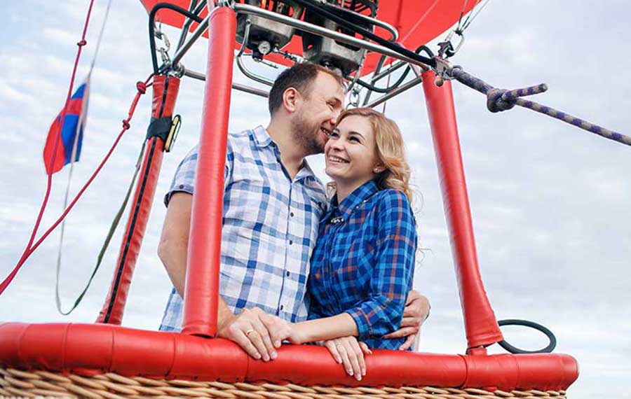 happy couple smiling in red hot air balloon basket with rigging and sky