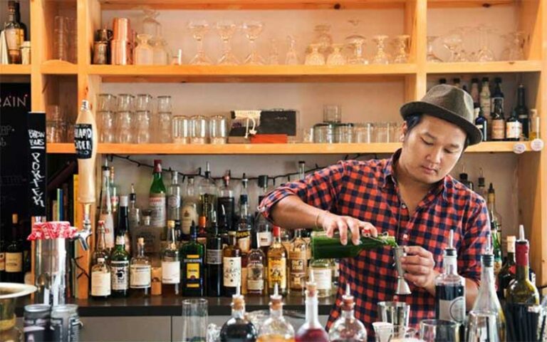 man mixing cocktail behind bar with bottles and glasses at grape grain exchange jacksonville