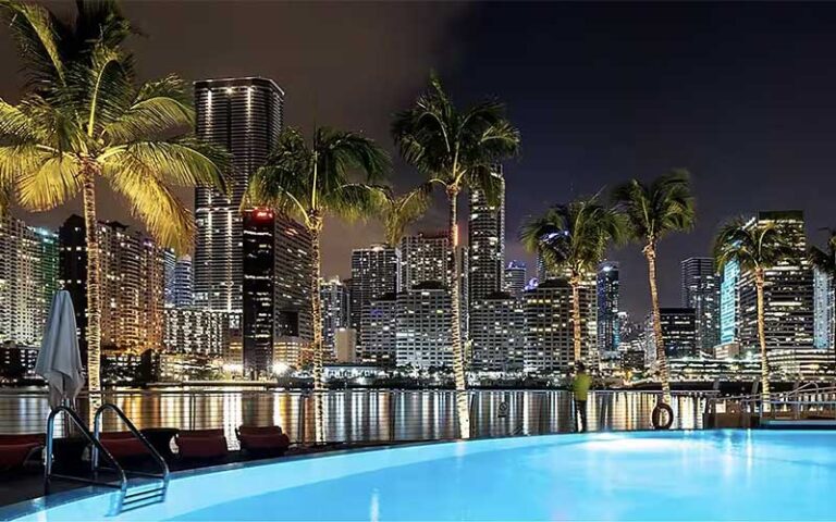 night at pool deck with blue water palm trees and city skyline at mandarin oriental miami