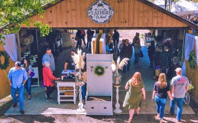 outdoor market in open barn with weathered wheel sign and shoppers at diamond d ranch jacksonville