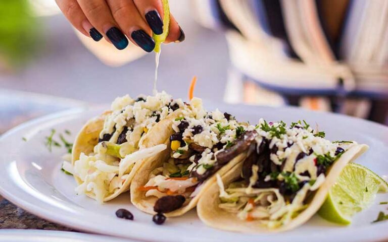 row of seafood soft tacos with hand squeezing lime at montys coconut grove miami