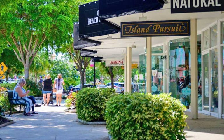 row of shops with black awnings tree and bushes along sidewalk at st armands circle sarasota