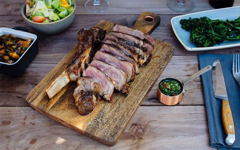 steak on board with spinach salad sides on wood table at novecento miami