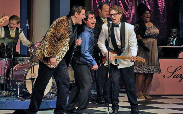 three musicians singing into mic on stage for buddy holly at alhambra theatre jacksonville