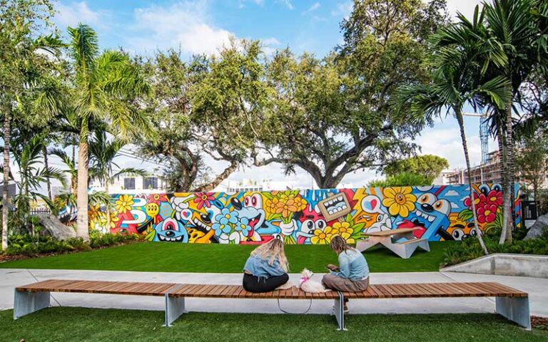 two girls and dog sitting on bench with artistic mural at wynwood walls miami