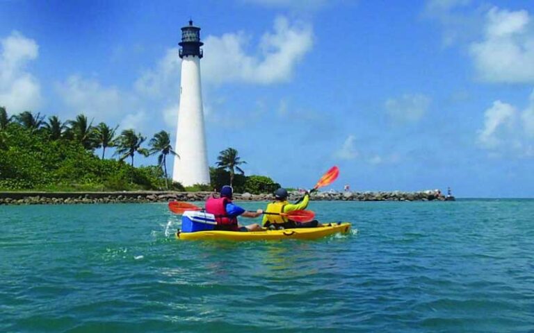 two people in kayak on bay with tree line coast and lighthouse at bill baggs cape florida state park miami