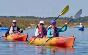 two riders in tandem kayak and one rider in single kayak with other kayaks behind and reeds at kayak amelia jacksonville