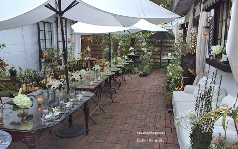 bricked patio with rows of tables and white umbrellas at garden room cafe at shoogie boogies sarasota