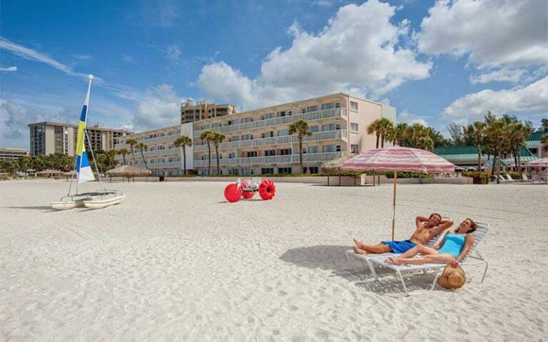 couple in chairs on beach with catamaran and pedalboat at sandcastle resort lido beach sarasota