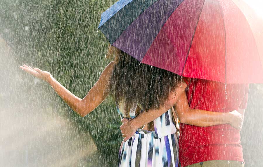 man and woman under umbrella facing away with womans arm extended to feel water with heavy rain