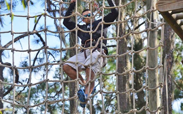 man with sunglasses climbing rope net at treeumph adventure course bradenton