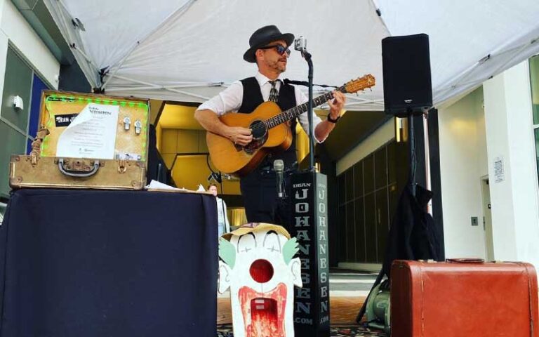 nicely dressed man with guitar performing at microphone in covered stage at sarasota farmers market