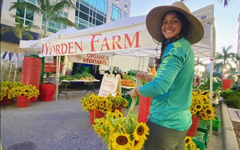 woman smiling with sunflowers and worden farm sign at sarasota farmers market