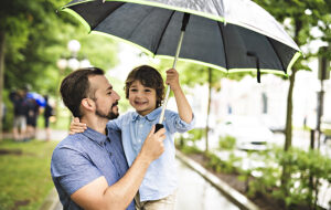 father holding young son with green and black umbrella in park