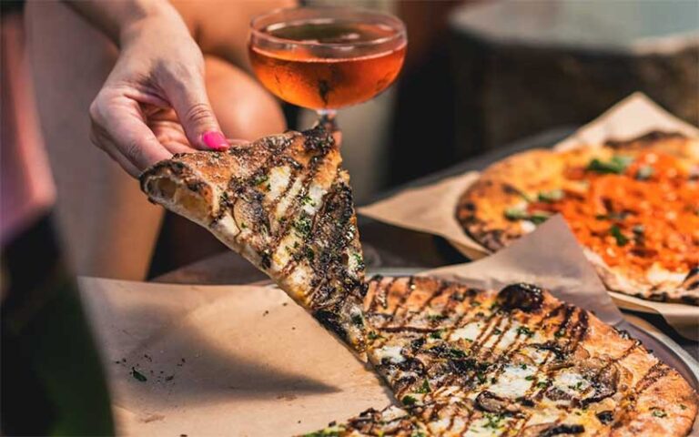 womans hand picking up pizza slice with wine glass at rooftop 1wlo ft lauderdale