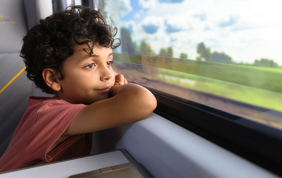 boy gazing out train window as scenery whips by on brightline train