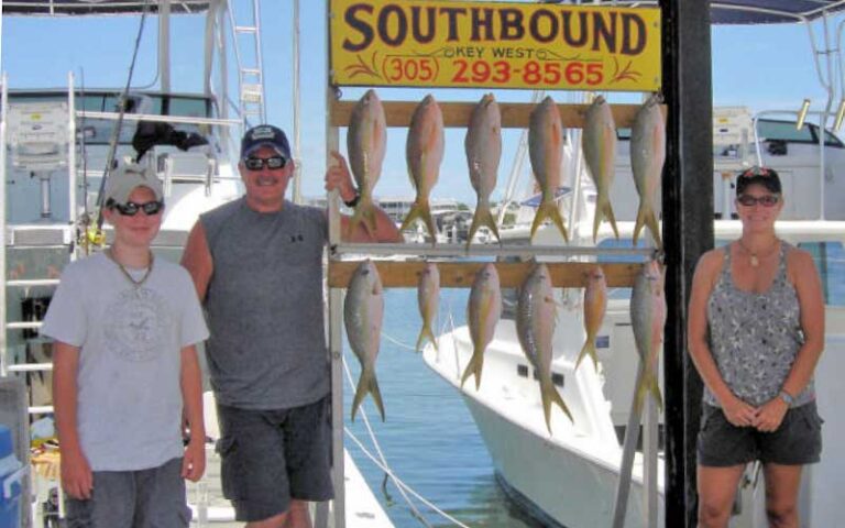 family posing on dock with red fish and southbound sign at historic charter boat row key west