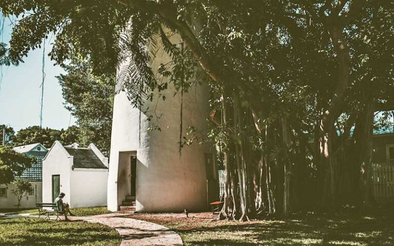 person on bench near trees and base of lighthouse at key west lighthouse and keepers quarters museum