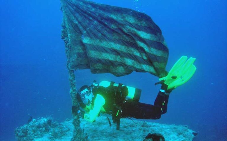 scuba diver holding eroded flag on bow at uss spiegel grove wreck key largo