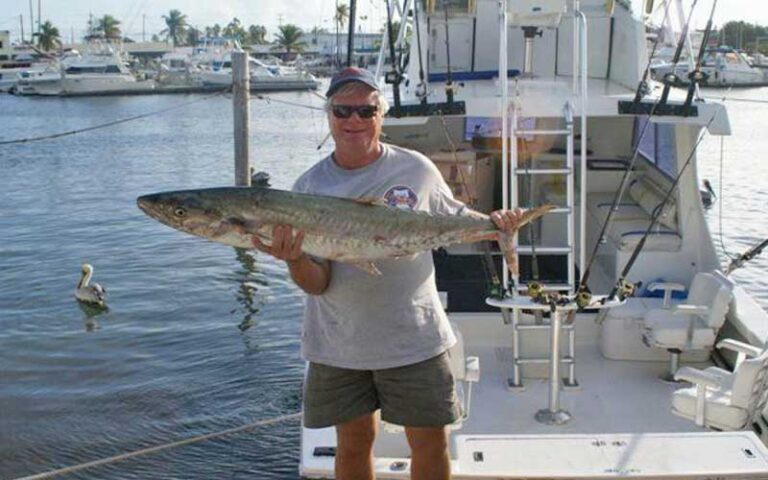 smiling man holding large fish with marina behind at historic charter boat row key west