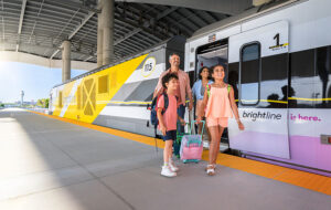 tourist family smiling exiting train and walking on platform with airport background at brightline train station