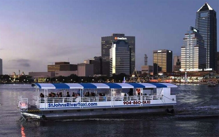 boat on river at dusk with lit up buildings at st johns river taxi jacksonville