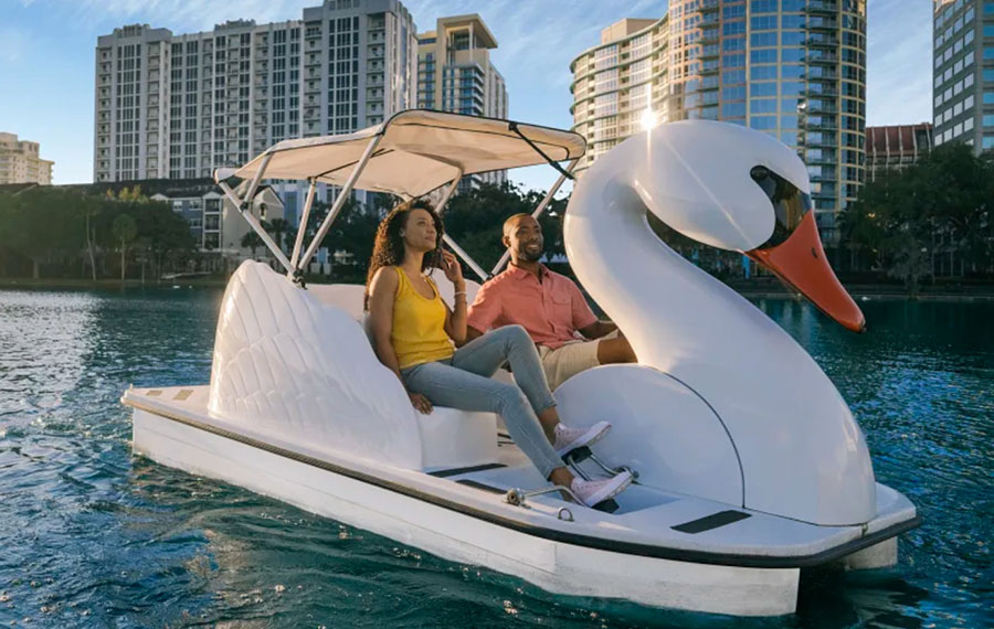 couple in swan pedal boat on water with high rise buildings behind lake eola orlando