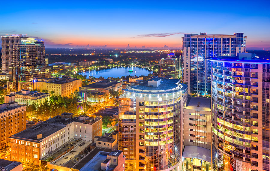 downtown skyline at dusk with colorful lighted buildings and lake with fountain orlando