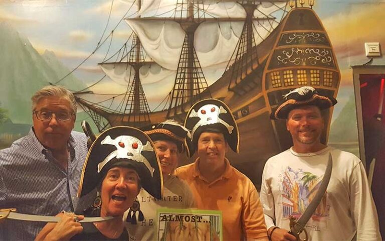 group with pirate props posing with pirate ship mural at key west room escape