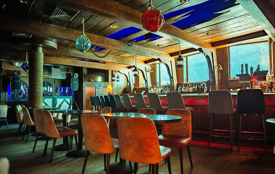 interior of sunken ship themed bar with seating and porthole style windows aquarium at the wreck bar