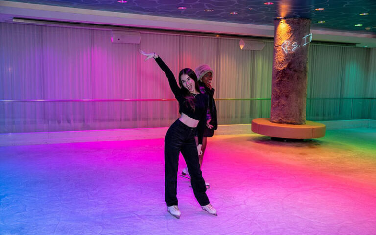 laughing girls ice skating on rink with neon lighting and column at basement bowl and skate miami beach edition