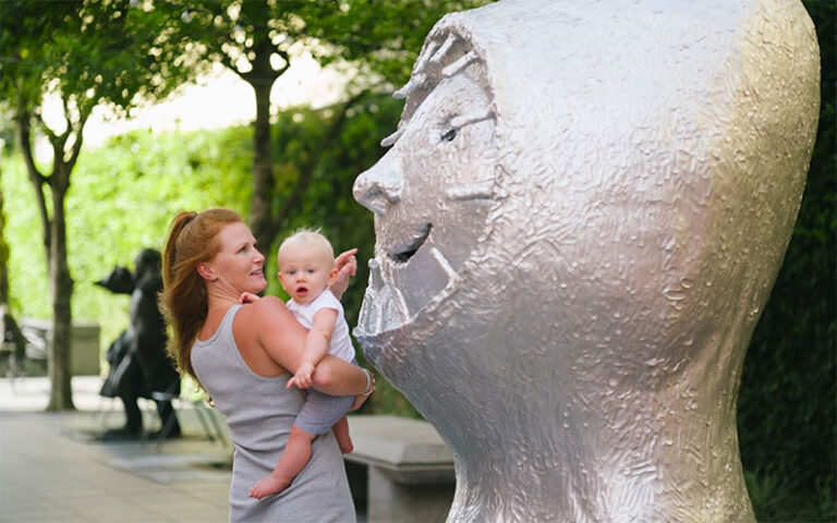 mom holding child pointing at face sculpture outdoor at boca raton museum of art