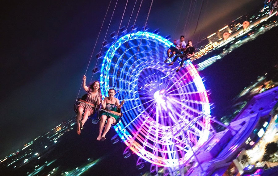 pair of young ladies on swing ride with ferris wheel behind at night orlando starflyer international drive