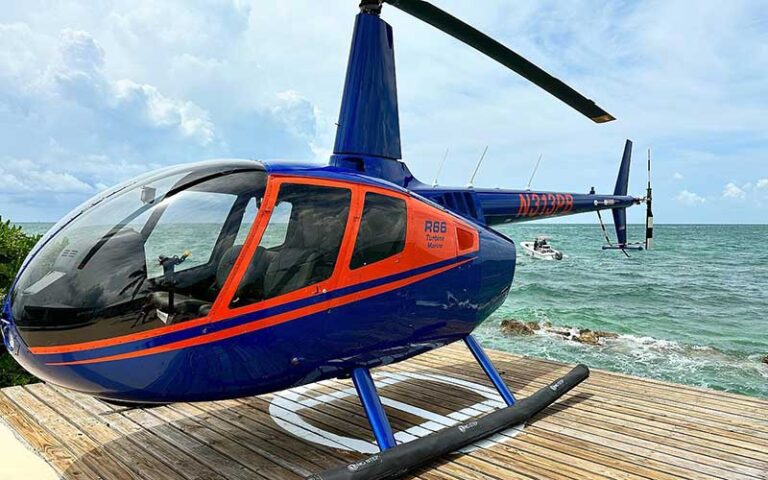 red and blue helicopter on dock with boat behind at keys helicopter tours marathon