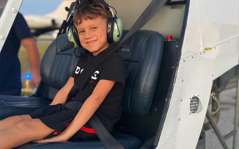 smiling boy seated in helicopter with safety belt and earphones at keen fly fort lauderdale
