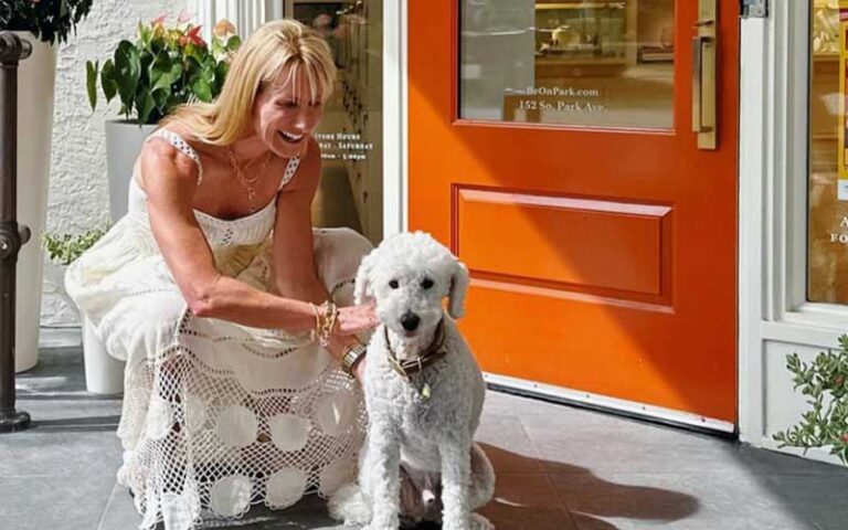 woman seated with white poodle in front of shop at park avenue district winter park