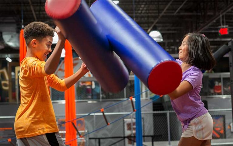 boy and girl joust with foam batons in ninja course at sky zone trampoline park fort myers
