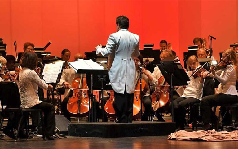conductor leading orchestra on stage with red background at gulf coast symphony fort myers