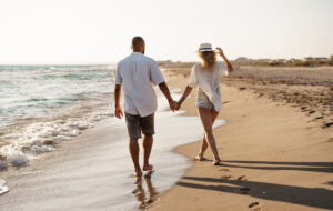 couple walking hand in hand on beach with long shadows